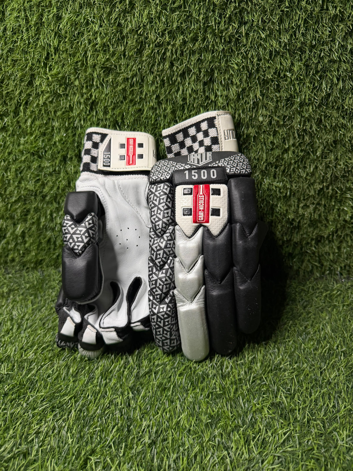A pair of black Gray Nicolls gloves with a green background